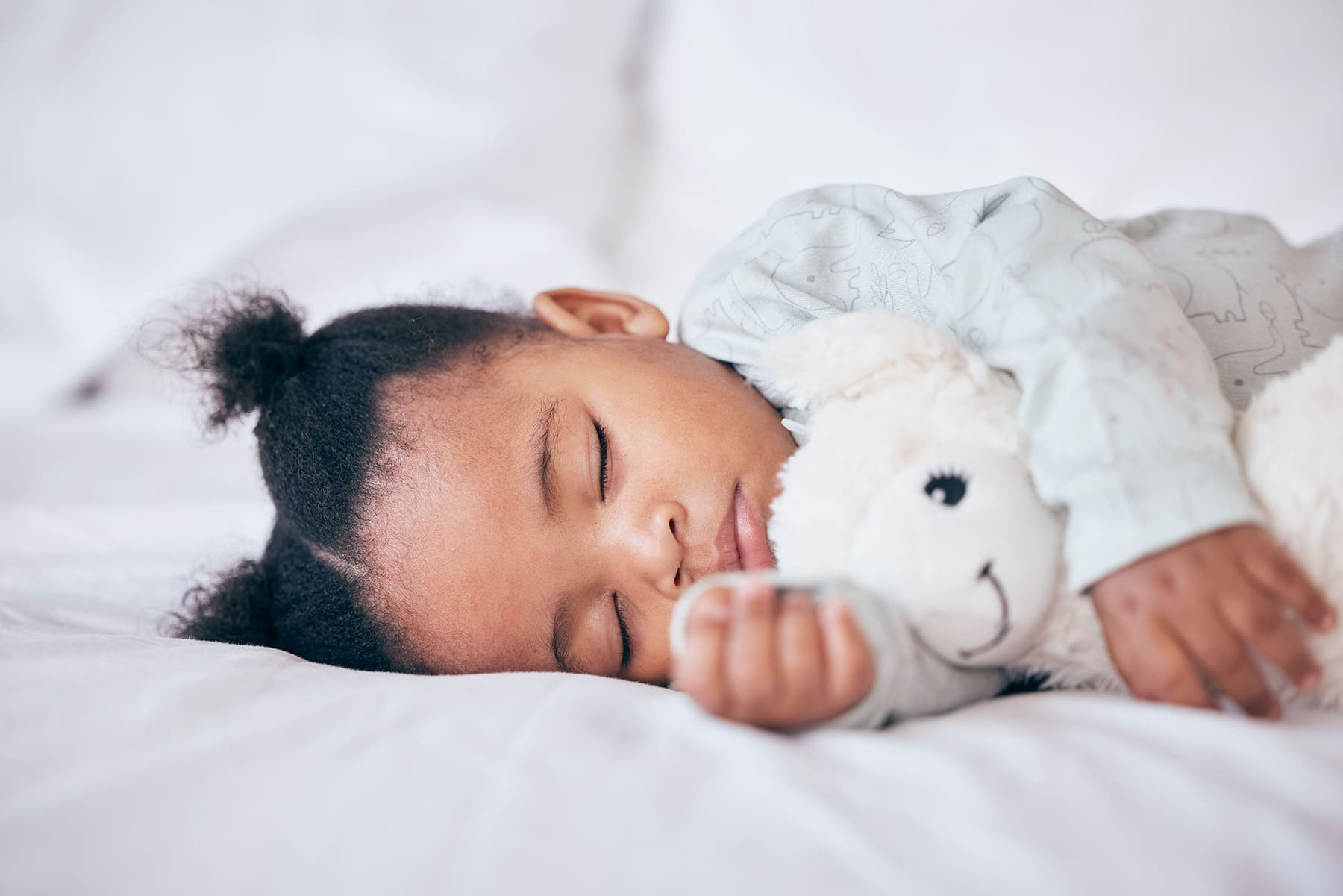 Toddler peacefully sleeping on a white bed while cuddling a soft, plush stuffed animal.