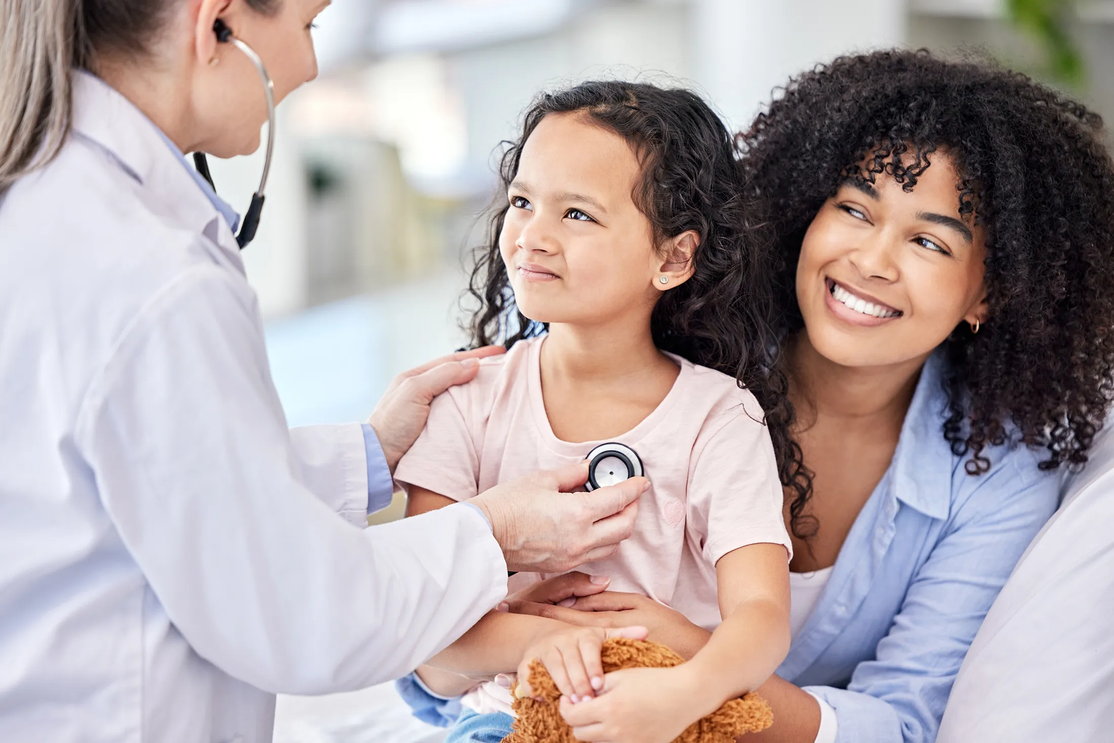 Smiling mother with daughter as a pediatrician uses stethoscope during a checkup.