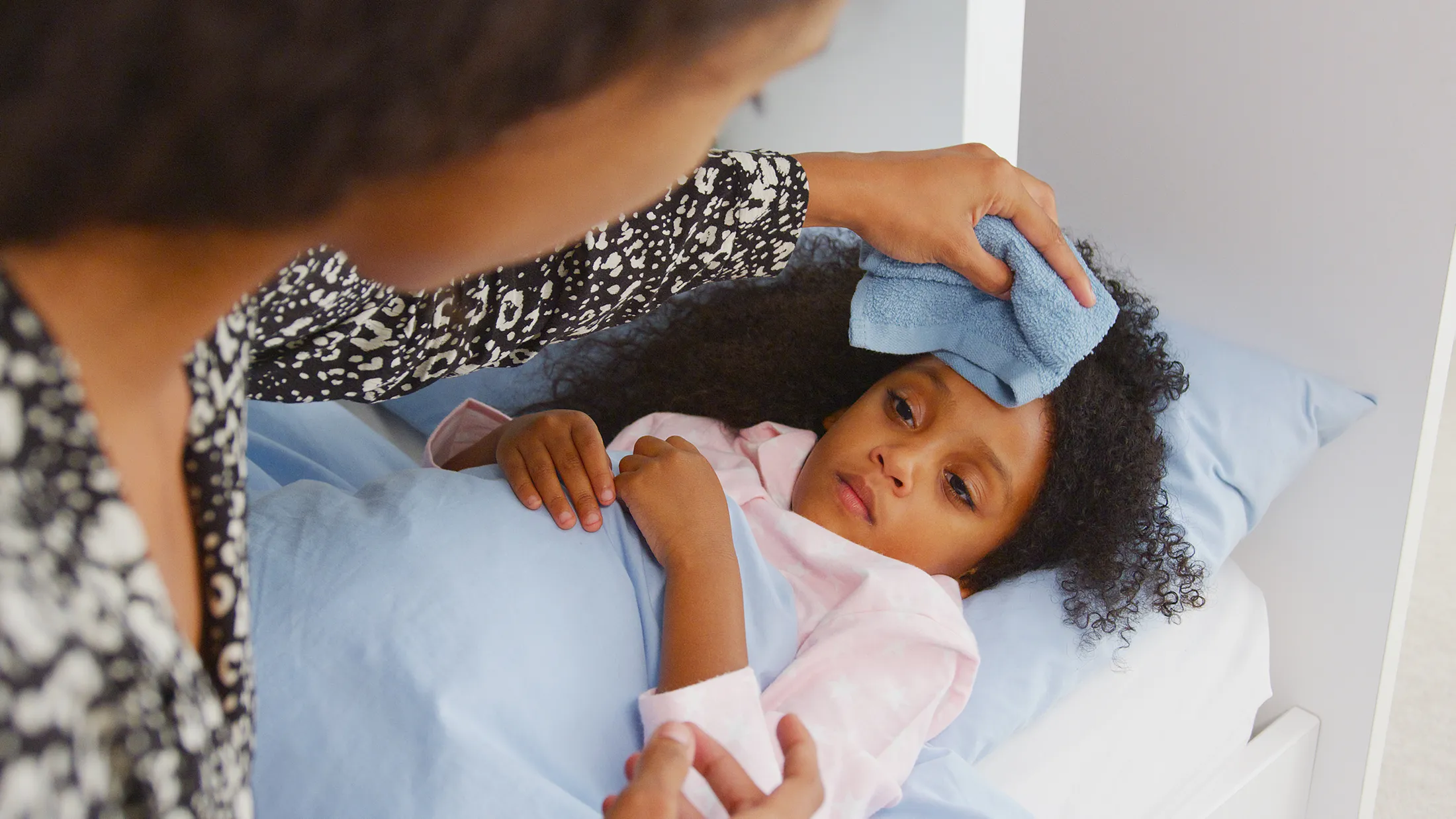Mother caring for her sick daughter in bed, illustrating flu prevention tips for babies and toddlers and the importance of the flu vaccine for families.
